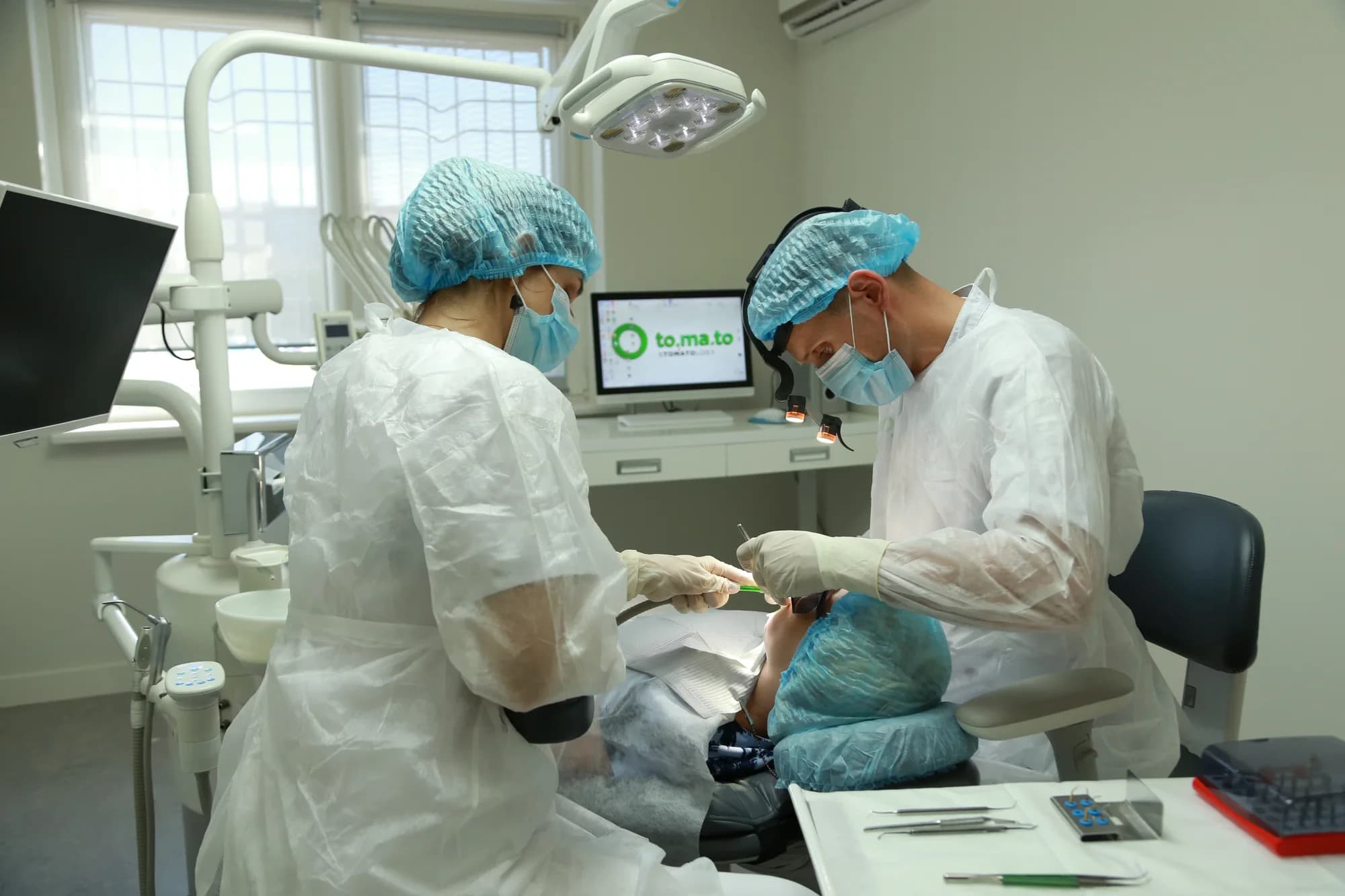 Хирург и ассистент проводят имплантацию в кабинете клиники to.ma.to